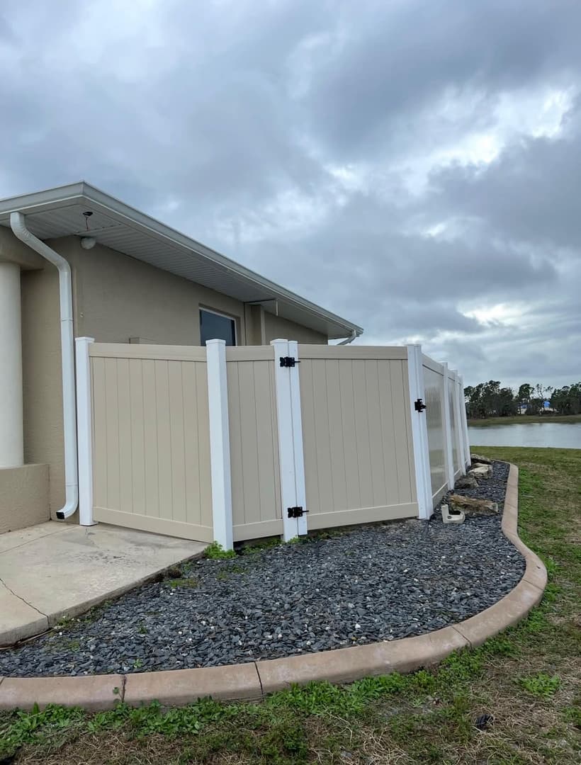 Tan vinyl privacy fence with decorative gravel border in North Port