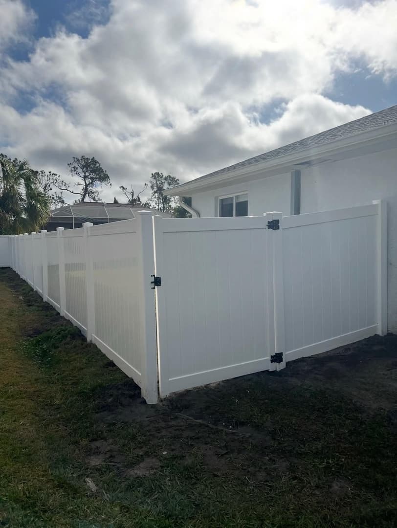 White vinyl privacy fence with gate installed along house